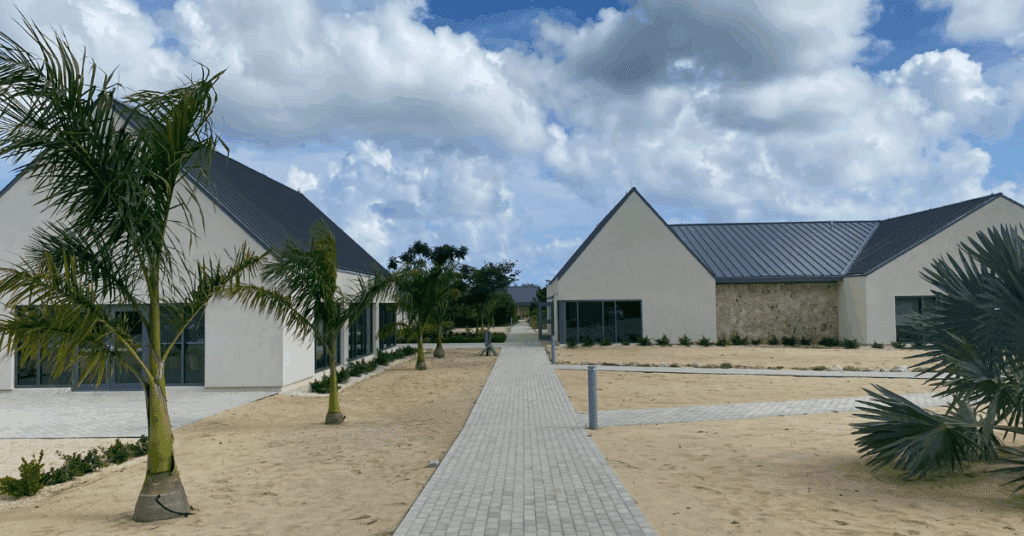 Closer view of two exterior buildings at the Poinciana Rehabilitation Centre, surrounded by trees and sand.