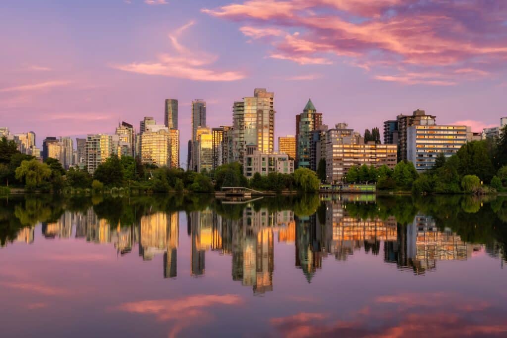 Tall buildings along the Vancouver waterfront reflect on the water under a pink sky